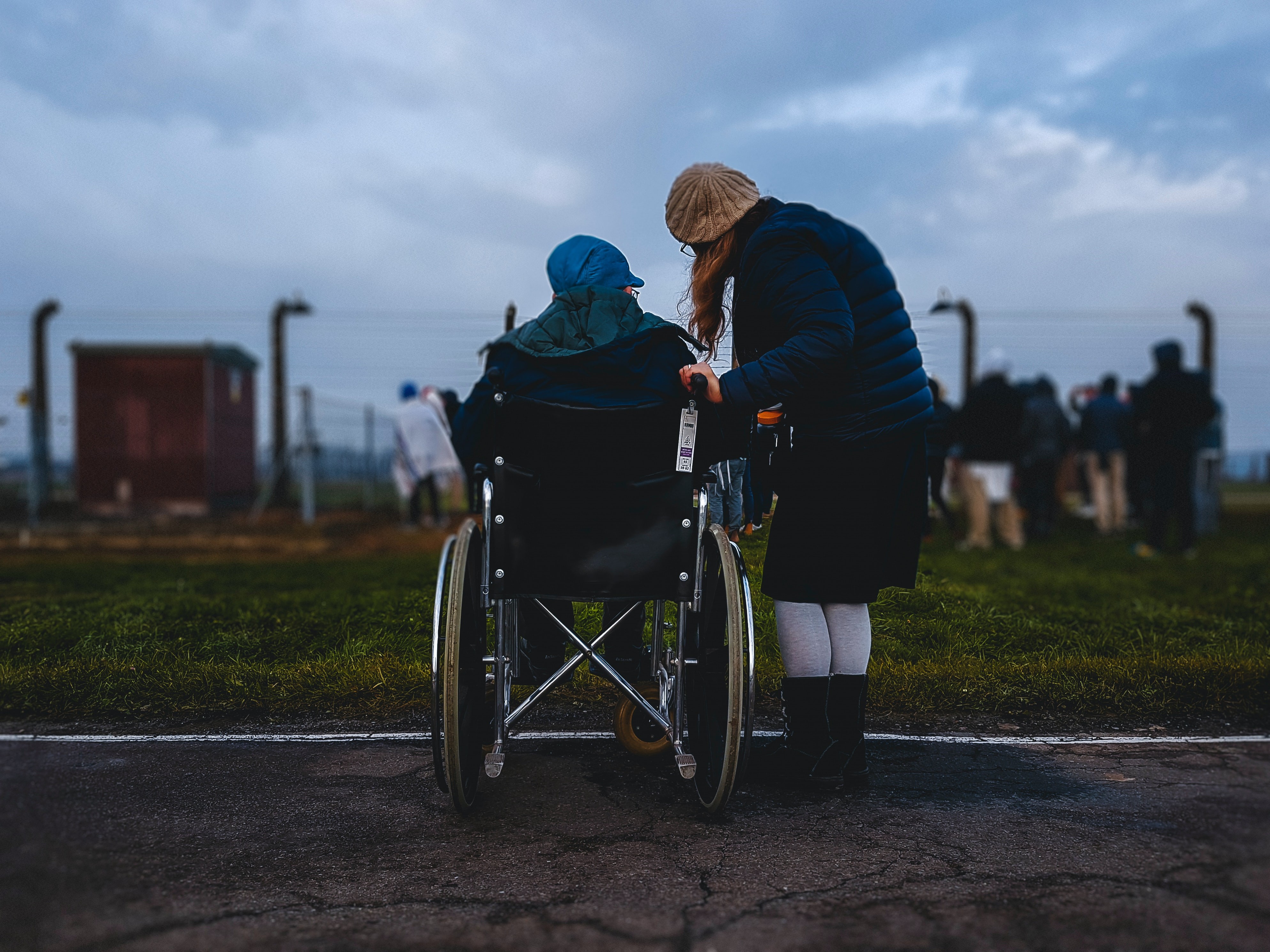photo of two people outside, one in a wheelchair, and the other is stood beside them, and they're talking